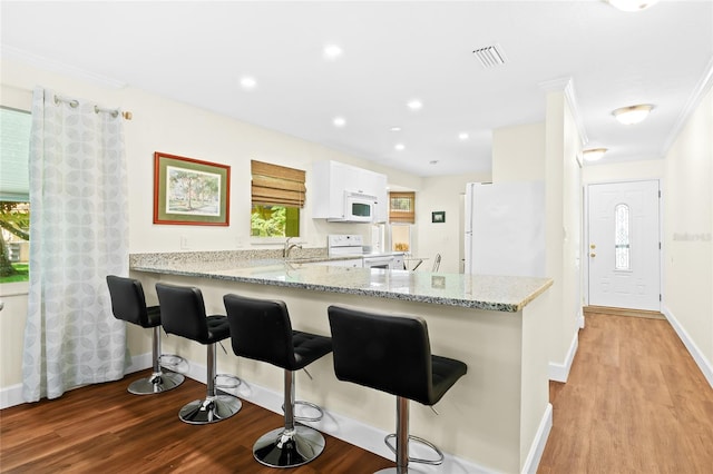 kitchen with white appliances, light stone countertops, a breakfast bar area, white cabinetry, and light hardwood / wood-style floors