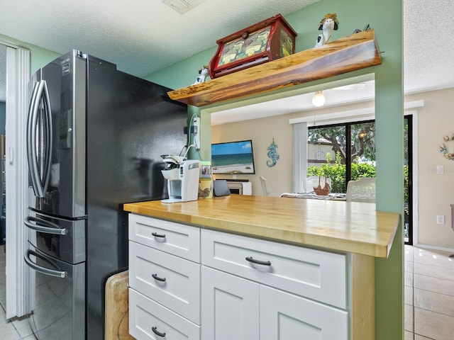 kitchen with a textured ceiling, light tile patterned floors, stainless steel fridge, and white cabinetry