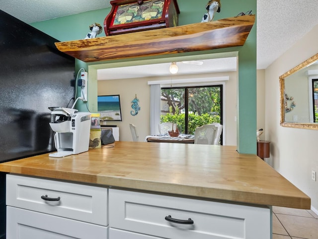 kitchen featuring wooden counters, light tile patterned floors, white cabinetry, and a textured ceiling