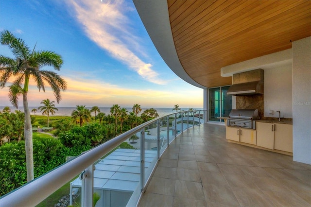 balcony at dusk with a water view, an outdoor kitchen, grilling area, and a sink