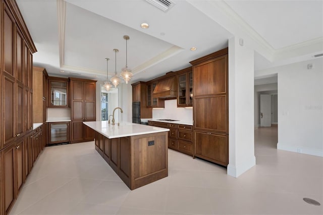 kitchen with premium range hood, a tray ceiling, a kitchen island with sink, pendant lighting, and light tile patterned floors