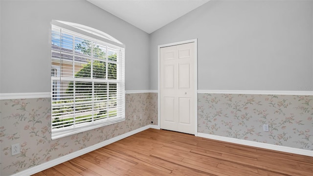 empty room featuring vaulted ceiling, a healthy amount of sunlight, and light hardwood / wood-style flooring