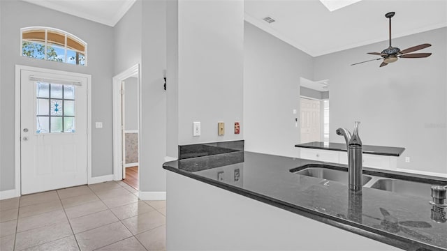 kitchen featuring light tile patterned flooring, ornamental molding, sink, and dark stone countertops