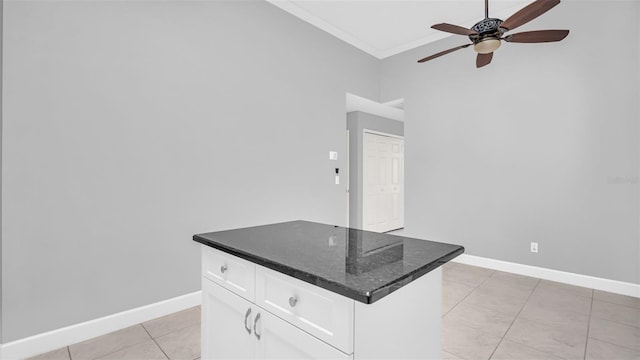 kitchen with light tile patterned flooring, ornamental molding, ceiling fan, dark stone counters, and white cabinets