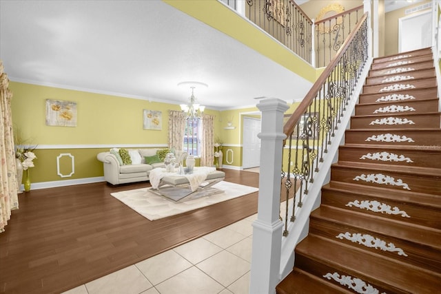 interior space featuring an inviting chandelier, a towering ceiling, wood-type flooring, ornamental molding, and ornate columns