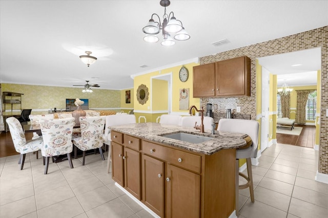 kitchen with light tile patterned flooring, sink, light stone counters, a center island with sink, and pendant lighting