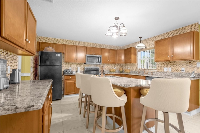 kitchen with decorative light fixtures, a center island with sink, light tile patterned floors, appliances with stainless steel finishes, and decorative backsplash