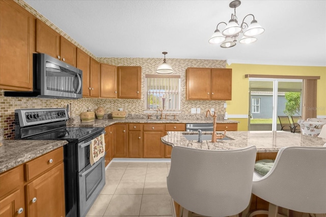 kitchen with light tile patterned flooring, appliances with stainless steel finishes, decorative backsplash, hanging light fixtures, and light stone counters