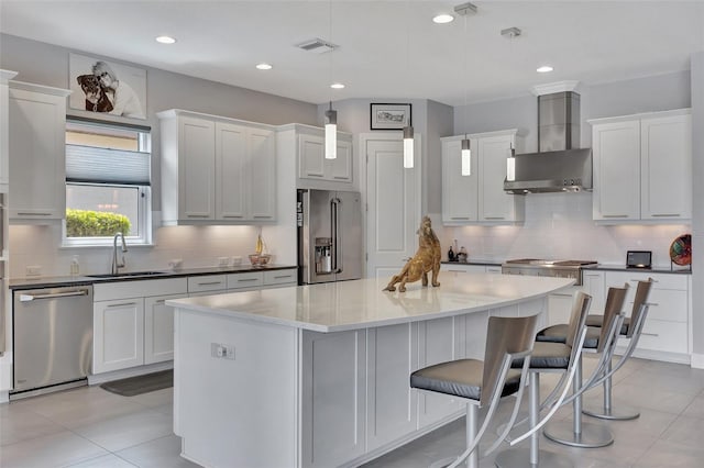 kitchen featuring wall chimney range hood, white cabinets, a kitchen island, appliances with stainless steel finishes, and sink