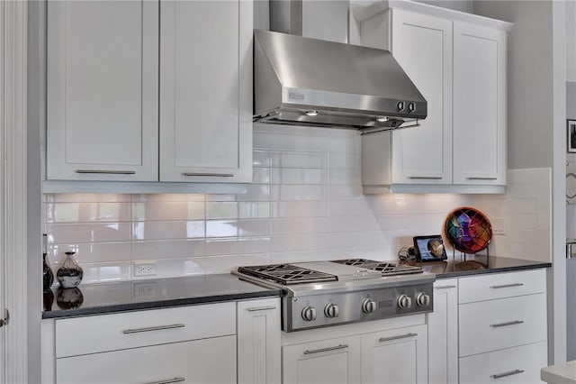 kitchen with white cabinets, backsplash, stainless steel gas stovetop, dark stone counters, and wall chimney exhaust hood