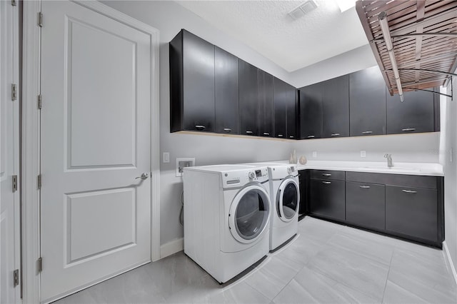 washroom with sink, washer and clothes dryer, a textured ceiling, and cabinets