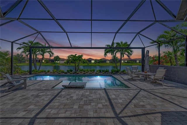 pool at dusk featuring a patio area, a water view, and glass enclosure