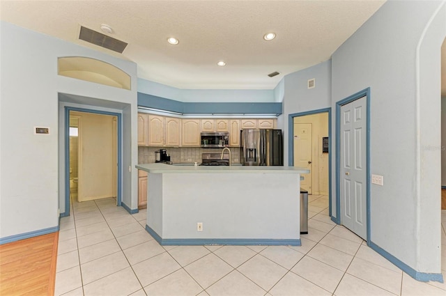 kitchen with a textured ceiling, an island with sink, light tile patterned floors, backsplash, and appliances with stainless steel finishes