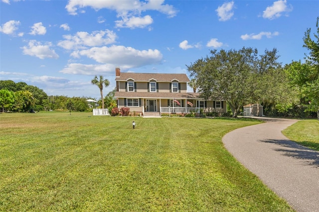 view of front facade with a porch, a front yard, a chimney, and aphalt driveway