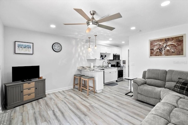 living room with ceiling fan, sink, and light wood-type flooring