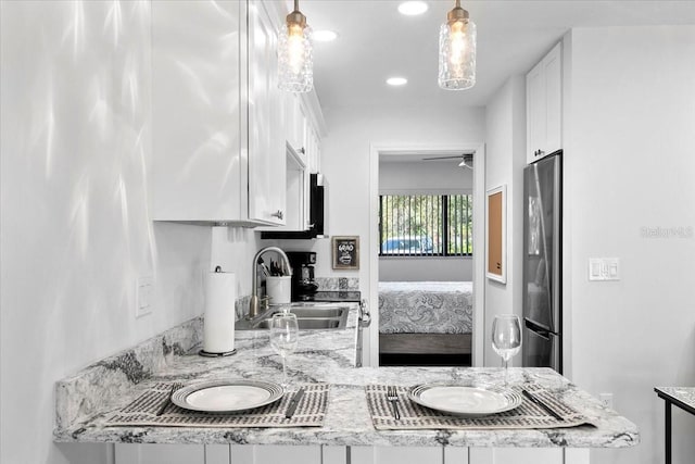 kitchen with stainless steel refrigerator, decorative light fixtures, sink, white cabinets, and light stone counters