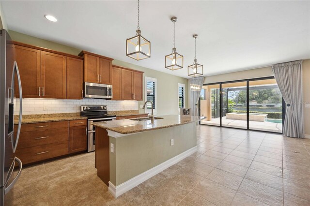 kitchen featuring appliances with stainless steel finishes, a kitchen island with sink, pendant lighting, light tile patterned floors, and tasteful backsplash