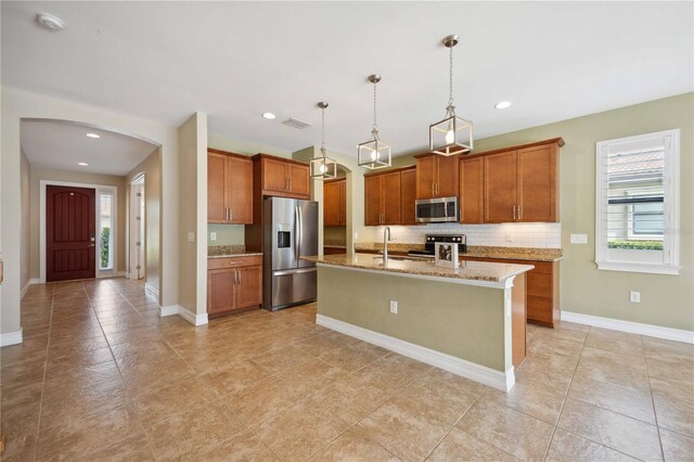 kitchen featuring pendant lighting, light tile patterned floors, a kitchen island with sink, appliances with stainless steel finishes, and backsplash