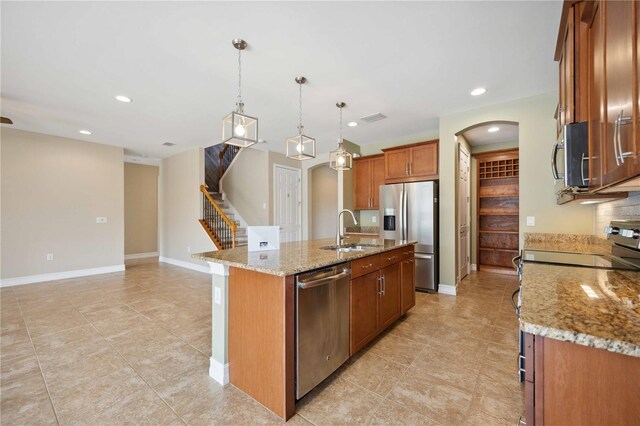 kitchen featuring light tile patterned flooring, stainless steel appliances, a kitchen island with sink, light stone counters, and sink