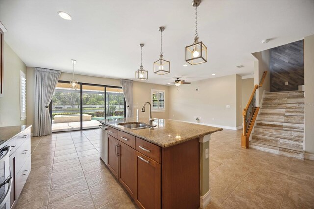 kitchen with light tile patterned floors, hanging light fixtures, light stone countertops, an island with sink, and sink