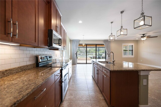 kitchen with light tile patterned floors, appliances with stainless steel finishes, a center island with sink, sink, and tasteful backsplash