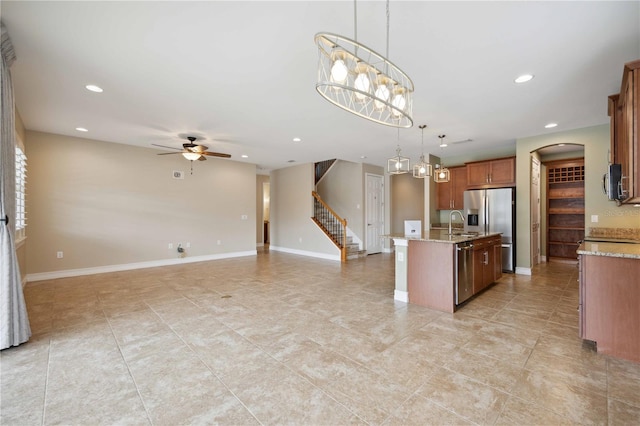 kitchen featuring ceiling fan with notable chandelier, light stone counters, pendant lighting, light tile patterned floors, and an island with sink