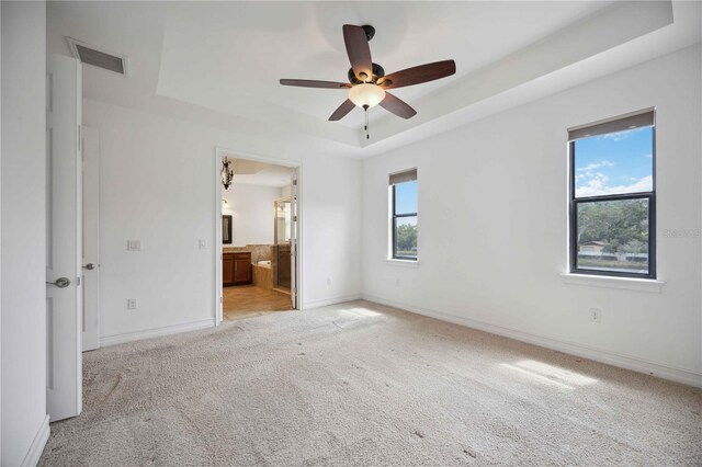 unfurnished bedroom with ceiling fan, light colored carpet, multiple windows, and a tray ceiling