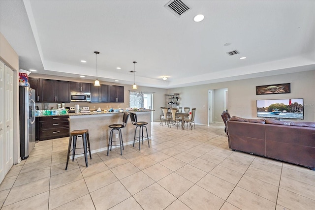 kitchen with dark brown cabinetry, a tray ceiling, a breakfast bar area, stainless steel appliances, and pendant lighting