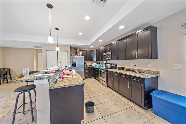 kitchen with a raised ceiling, a breakfast bar, a center island with sink, light tile patterned flooring, and stainless steel appliances