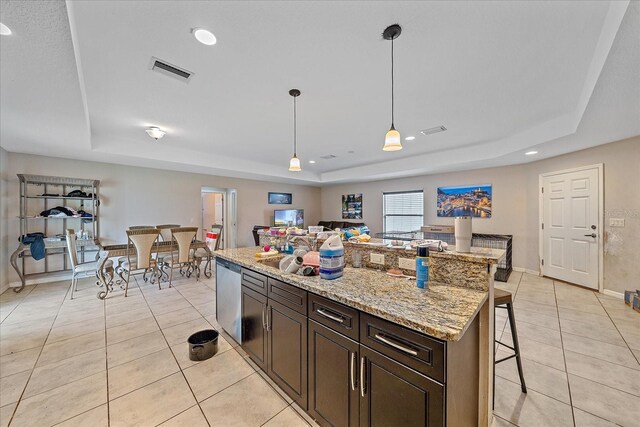 kitchen with a raised ceiling, a kitchen breakfast bar, hanging light fixtures, light stone counters, and light tile patterned floors