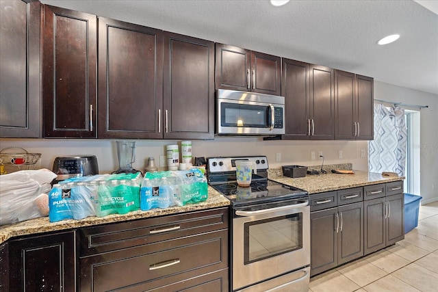 kitchen with stainless steel appliances, dark brown cabinets, light stone counters, a textured ceiling, and light tile patterned floors