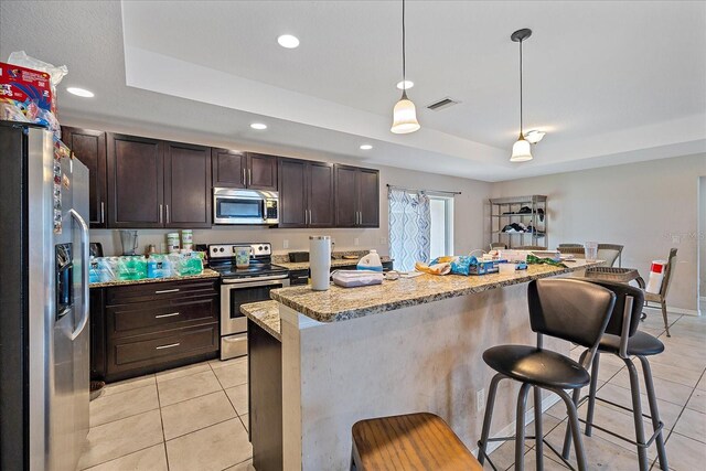 kitchen featuring stainless steel appliances, decorative light fixtures, light stone counters, light tile patterned floors, and a kitchen breakfast bar