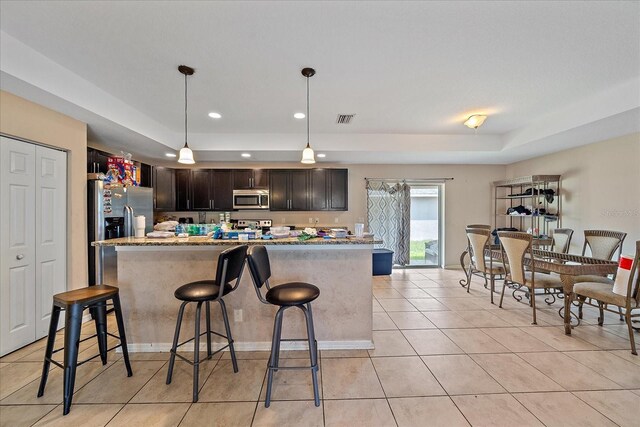 kitchen featuring light tile patterned flooring, dark brown cabinetry, light stone countertops, stainless steel appliances, and pendant lighting