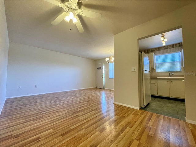 unfurnished living room with sink, light wood-type flooring, and ceiling fan with notable chandelier