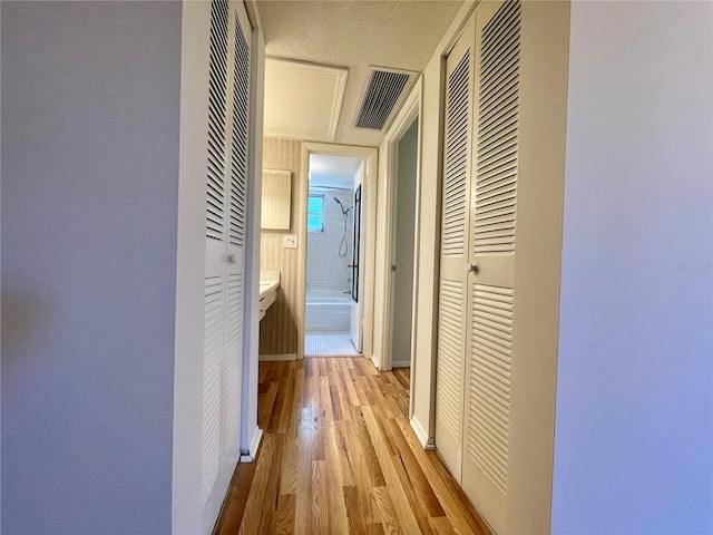 corridor featuring light wood-type flooring and a textured ceiling