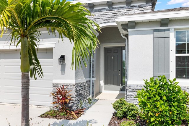 entrance to property featuring a garage, stone siding, and stucco siding