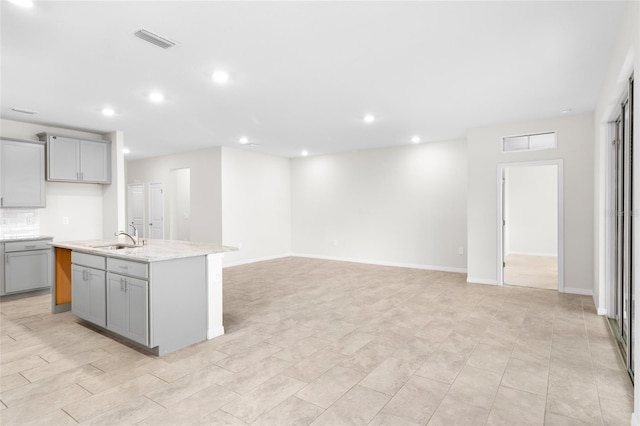 kitchen with a kitchen island with sink, gray cabinetry, visible vents, open floor plan, and light stone countertops