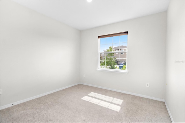 spare room featuring light colored carpet and baseboards