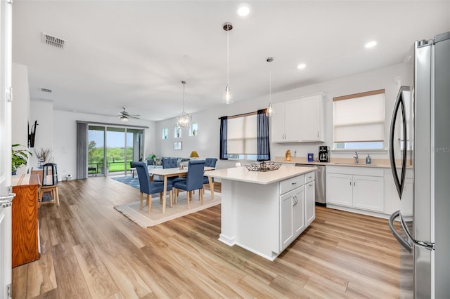 kitchen featuring white cabinetry, hanging light fixtures, a center island, light wood-type flooring, and stainless steel appliances