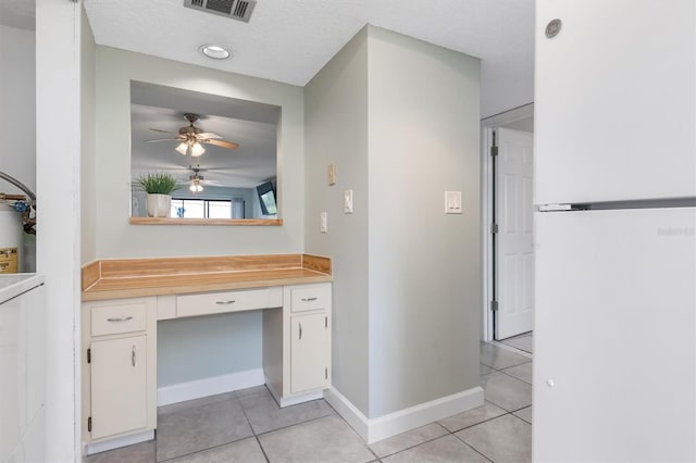 interior space featuring built in desk, white cabinets, white fridge, light tile patterned floors, and a textured ceiling