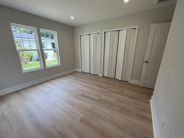 unfurnished bedroom with light wood-type flooring and multiple closets