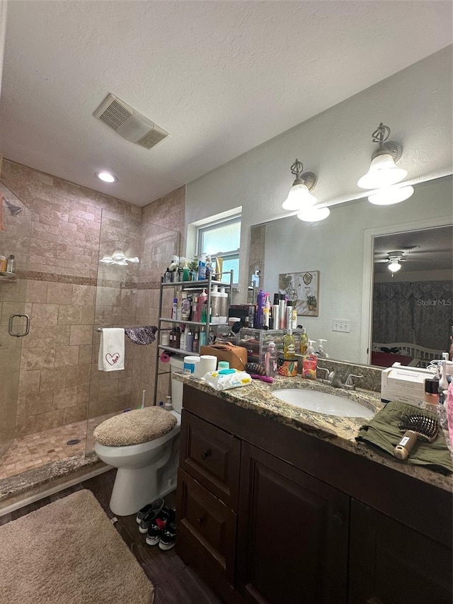 bathroom with toilet, vanity, a textured ceiling, ceiling fan, and a shower with door