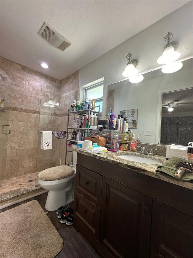 bathroom featuring ceiling fan, toilet, vanity, walk in shower, and a textured ceiling