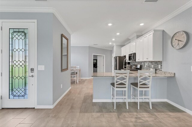 kitchen featuring backsplash, ornamental molding, a kitchen breakfast bar, white cabinets, and kitchen peninsula