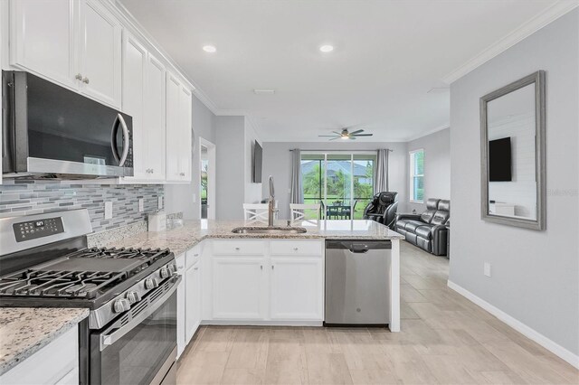 kitchen with sink, ornamental molding, light stone counters, stainless steel appliances, and white cabinets