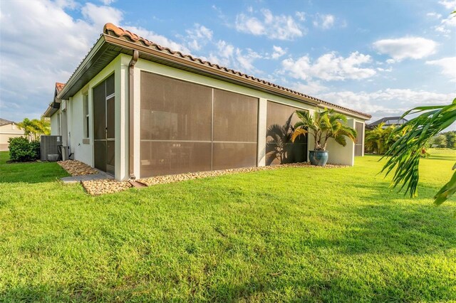 view of side of property with a yard, a sunroom, and cooling unit