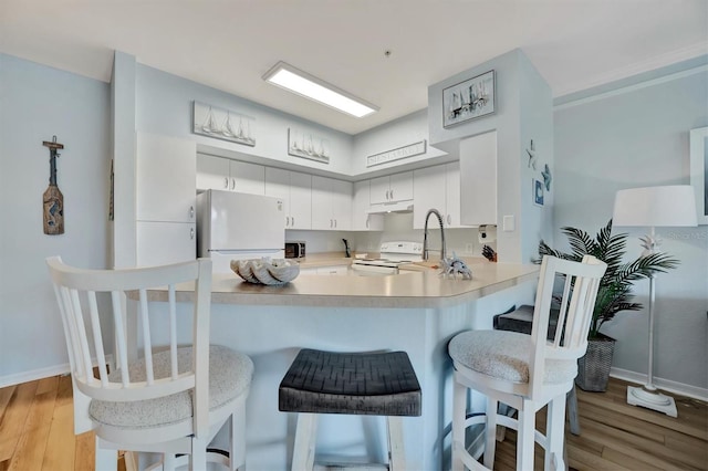 kitchen with kitchen peninsula, white cabinets, white appliances, and light wood-type flooring