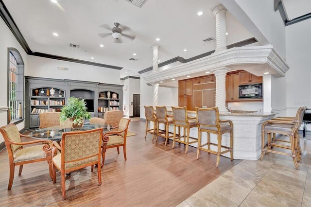 dining area with a towering ceiling, ornate columns, ornamental molding, ceiling fan, and light hardwood / wood-style flooring