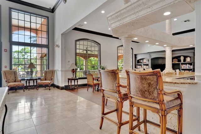 interior space with light tile patterned floors, crown molding, and decorative columns