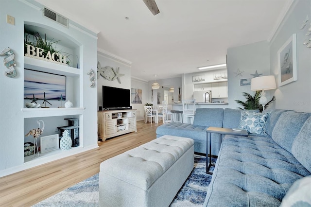 living room featuring built in shelves, light wood-type flooring, and ornamental molding